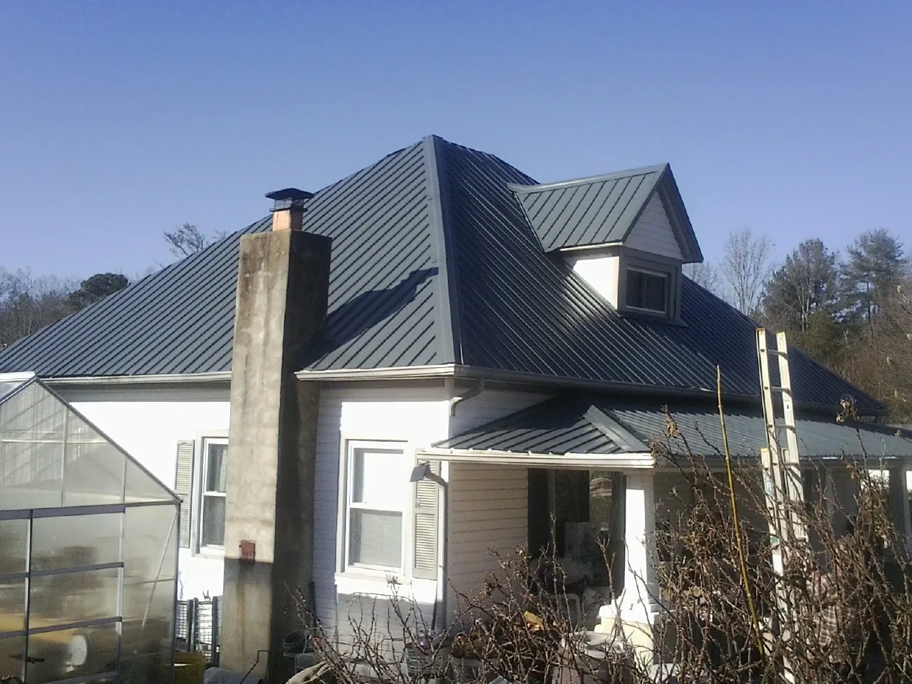 Dark blue standing seam metal roof on a white farmhouse with dormer — Slate & Tile Roof Repair by Roofing Brothers in Mamou