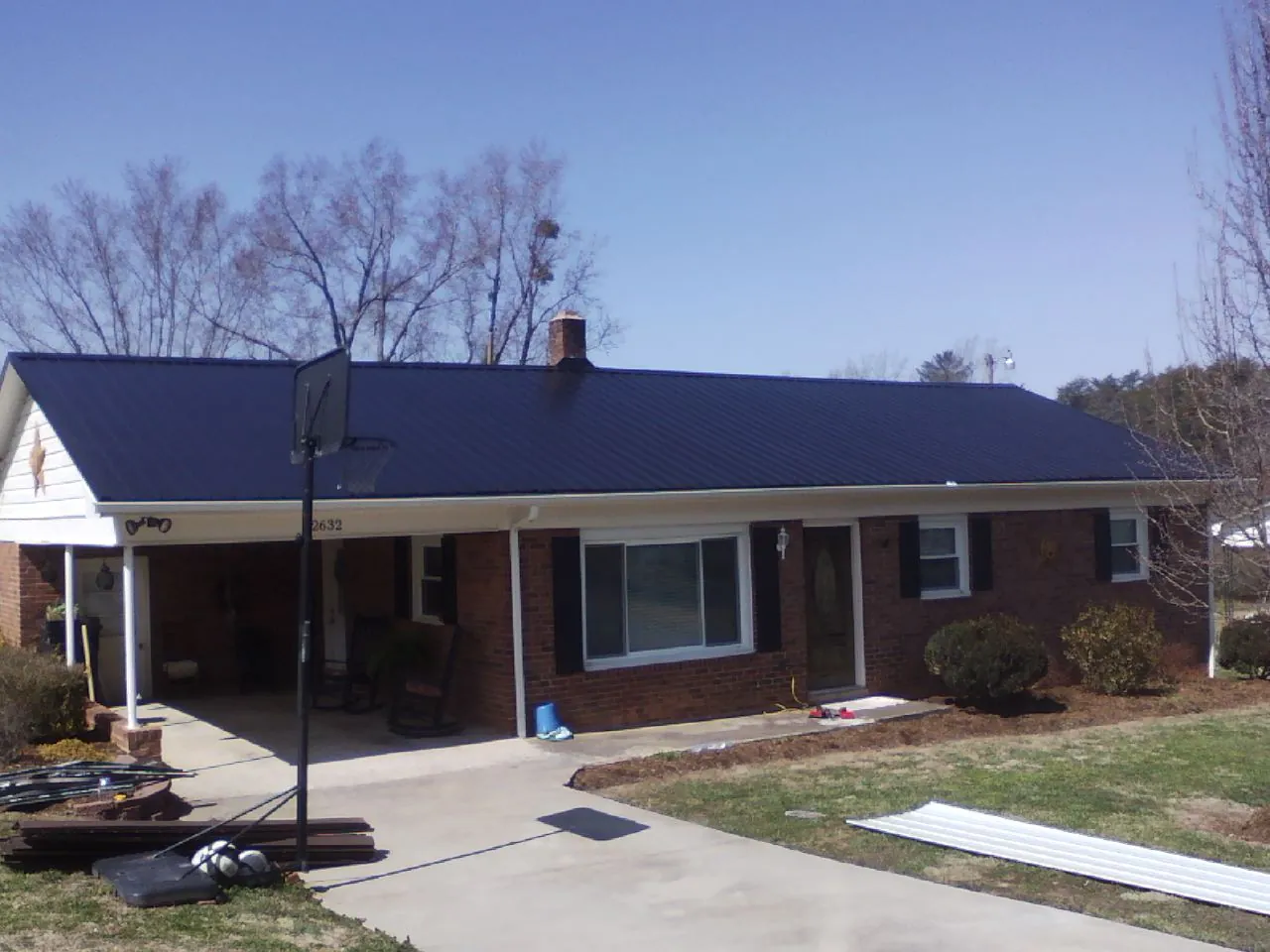Finished dark blue metal roof on a brick ranch with a carport in Mamou