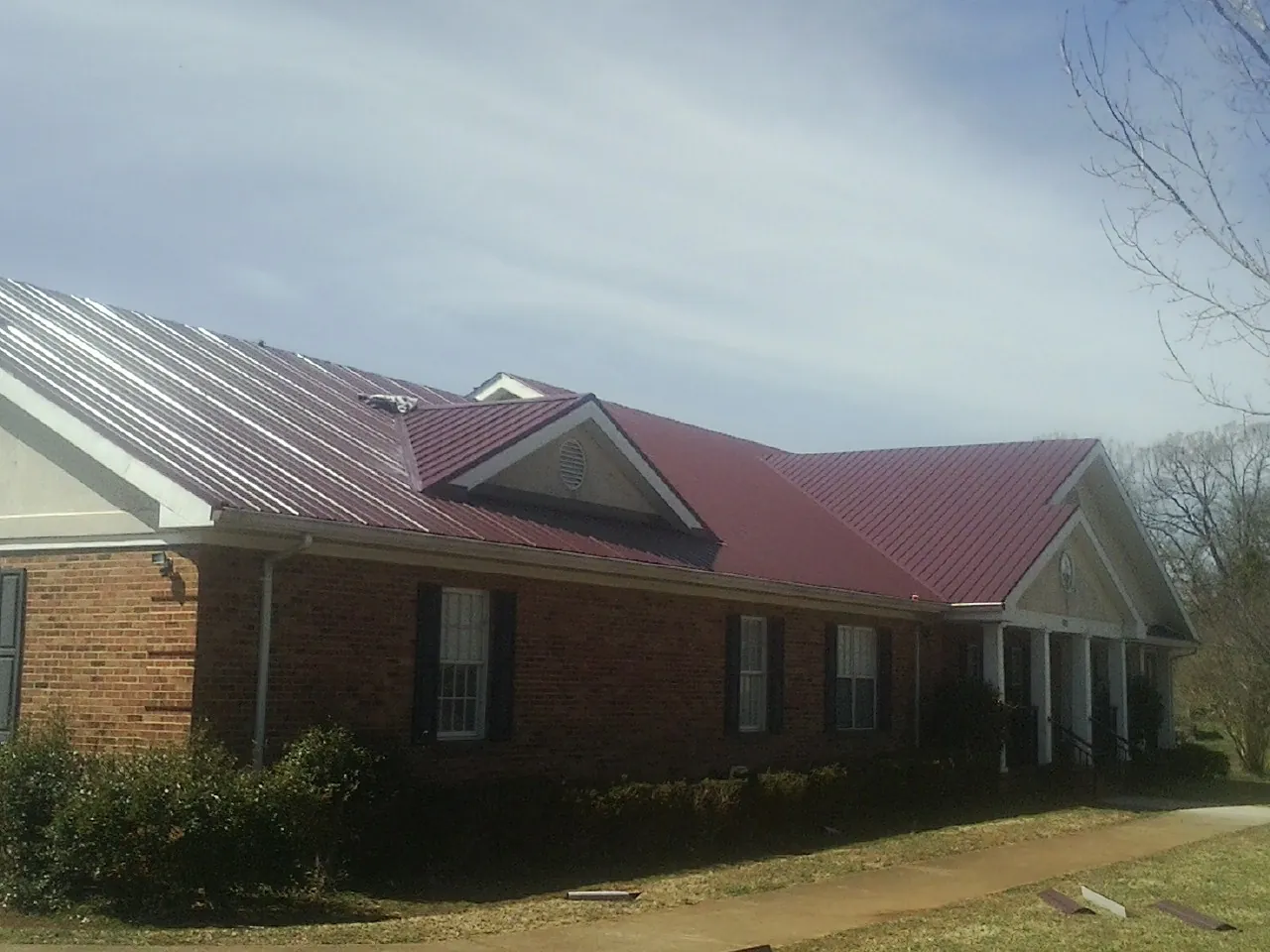 Red metal roof with gabled entries on a long brick building, from a Hail Damage Roof Repair job in Mamou