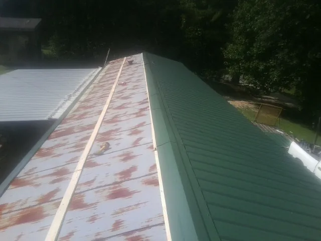 Old rusted panels beside newly installed green metal roofing — Wind Damage Roof Repair by Roofing Brothers in Mamou