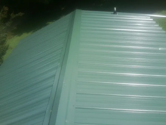 New green metal panels meeting at the ridge of a roof — Flat Roof Repair work by our crew in Mamou