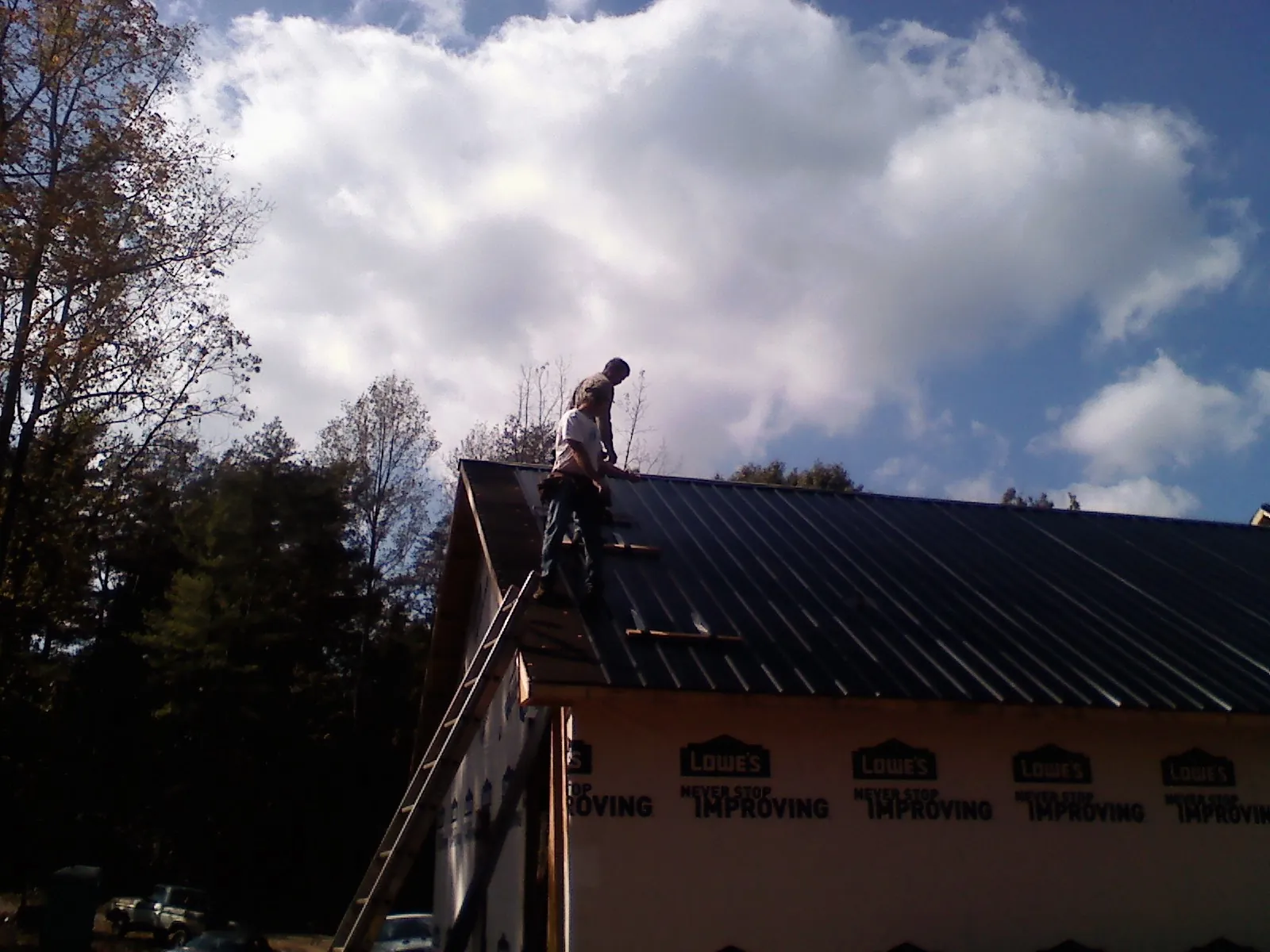 Roofer fastening dark metal panels high against a cloudy sky, from a Roof Inspection job in Mamou