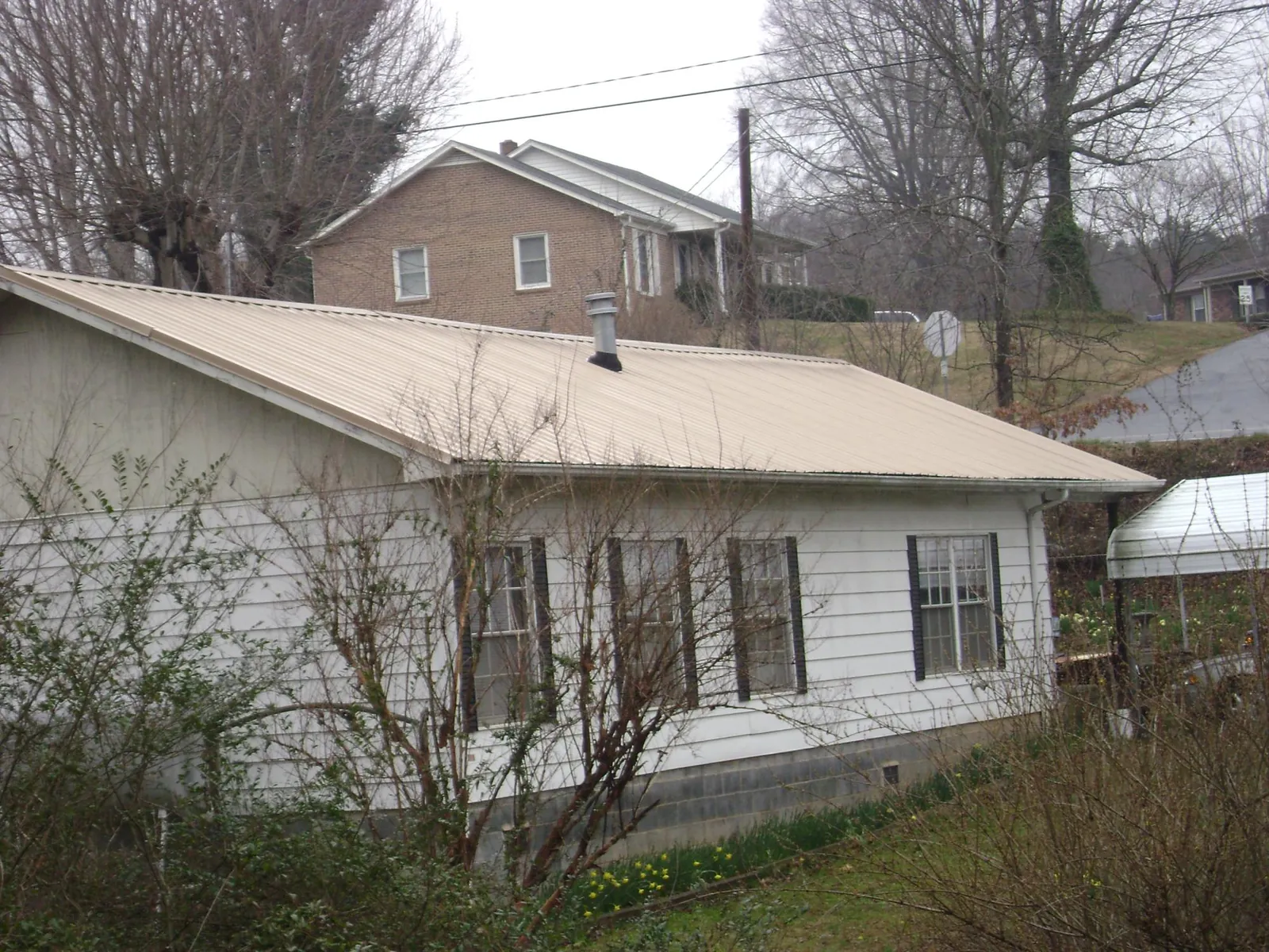 Tan metal roof on a white sided house set into a hillside — Commercial Roofing by Roofing Brothers in Mamou