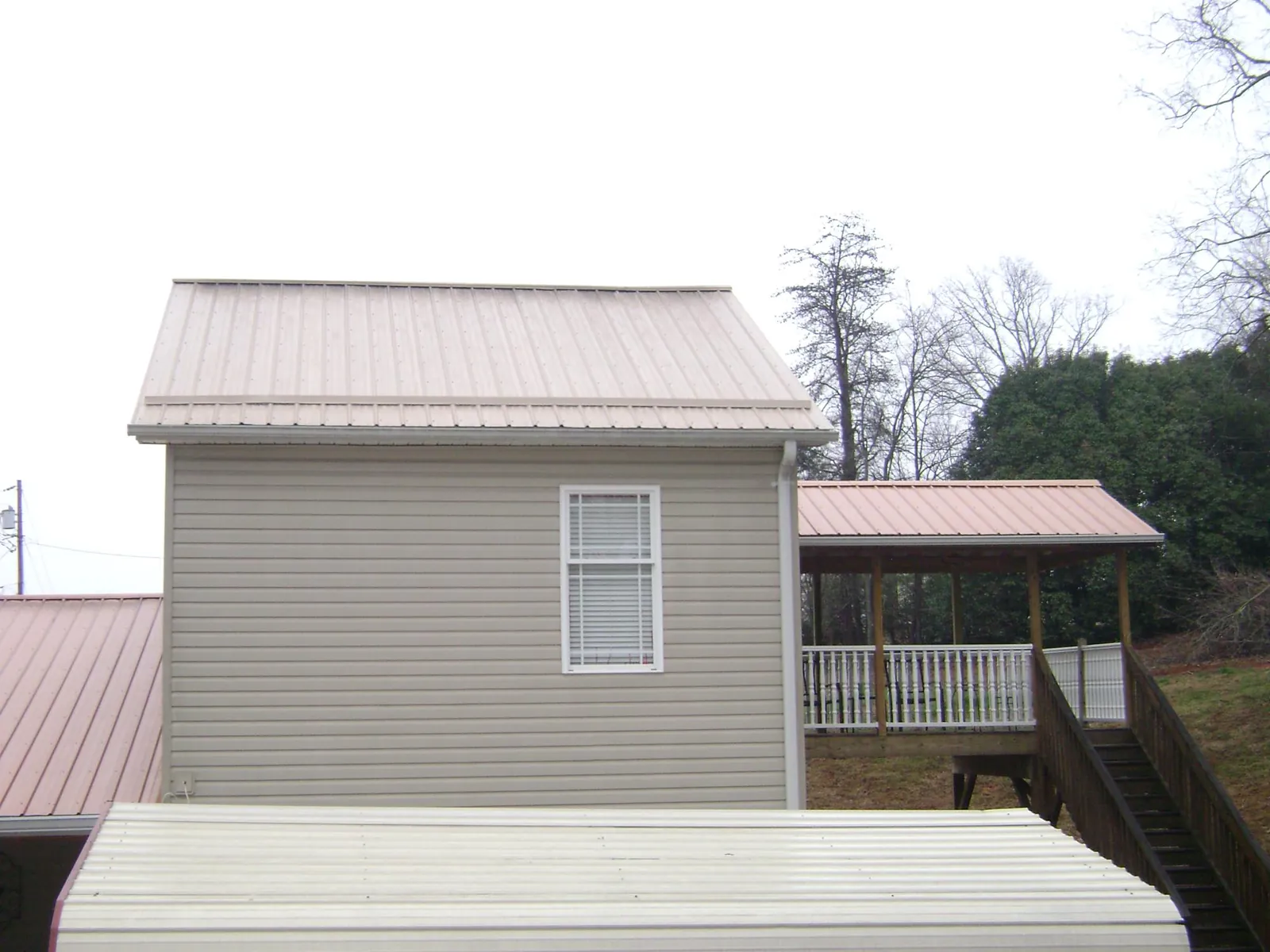 Tan metal roofs on a two story addition and attached porch, from a Roof Replacement job in Mamou